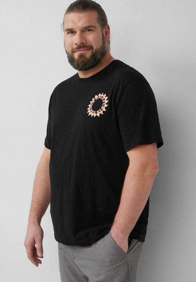 Zwarte katoenen t-shirt met een ronde, perzikkleurige zonnestraalafbeelding op de linkerborst. Relaxte pasvorm met korte mouwen en een ronde hals.
