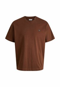 T-shirt en coton marron avec un col rond et des manches courtes. Présente un petit patch logo sur la zone du côté gauche de la poitrine. Texture lisse.