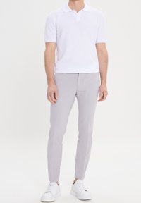 White short-sleeve polo shirt with a textured pattern, paired with light gray slim-fit trousers and white sneakers, standing on a neutral background.