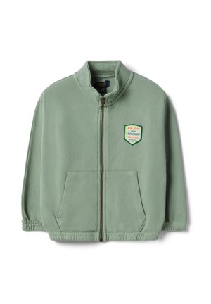 Giacca in pile verde chiaro con zip, due tasche frontali e una toppa colorata con la scritta "Enjoy Land Exploring Leader Adventure Camp" sul petto.