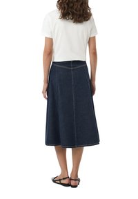 Spijkerrok met een uitlopende look, donker indigo kleur, zichtbare stikseldetails en een lengte tot halverwege de kuiten, gecombineerd met een wit T-shirt.