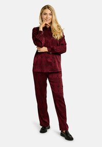 Vínovo vzorovaný saténový dvojdielny outfit, ktorý pozostáva z dlhorukávovej košele s golierom a zladených nohavíc. Čierne mokasíny dotvárajú celý look.