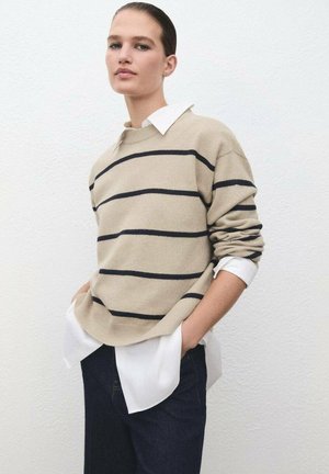 Suéter a rayas beige con líneas en marino, textura de punto, escote redondo, que se lleva encima de una camisa blanca, combinado con pantalones oscuros. Fondo liso.