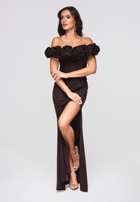 Langes schwarzes Kleid mit schulterfreiem Design und Blumenapplikationen. Schlitz auf der linken Seite, kombiniert mit transparenten Riemchenabsätzen.