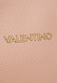 Du cuir texturé rose clair présentant un logo en relief « VALENTINO » en doré, avec une finition lisse et un motif grainé subtil.