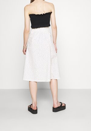 Haut sans manche smocké noir associé à une jupe midi blanche à fleurs. La jupe présente une texture douce et une silhouette évasée. Sandales à plateforme noires.