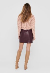 Pull en tricot à manches bouffantes rose, associé à une jupe en cuir bordeaux ajustée. Des bottes beiges jusqu'aux genoux complètent la tenue.