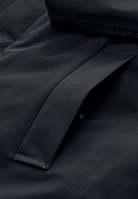 Detail tmavomodrého vrecka na bundu s klopou, ktorý zobrazuje hladkú látku a jemné šitie.