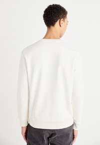 Felpa bianca con colletto rotondo, maniche lunghe e polsini a coste. Texture liscia. Cuciture visibili alle cuciture e all'orlo.