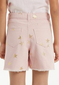 Růžové denimové kraťasy s trhaným lemem, pokryté zlatými hvězdicovými vzory. Mají dvě zadní kapsy a úzký pas.