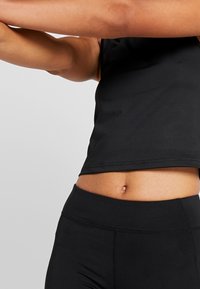 Haut noir sans manches au design ajusté, associé à un legging noir taille haute. Les deux sont confectionnés dans un tissu lisse et extensible.