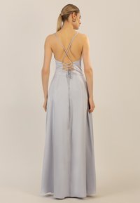 Langes hellblaues Abendkleid mit Kreuzdetails auf dem Rücken und Schnürakzenten. Schmale Träger und ein fließendes Rockdesign. Glatte Satinoberfläche.