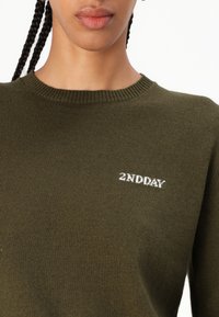 Olivengrønn genser laget av myk ull, med klassisk rund hals og hvit brodert logo "2NDDAY" på forsiden.