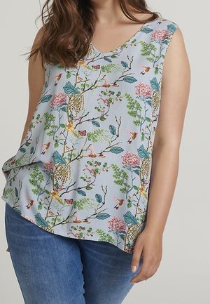 Mouwloze lichtblauwe blouse met kleurrijke bloem- en vogelpatronen gedragen met een blauwe spijkerbroek door een persoon die tegen een effen achtergrond staat.