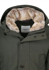 Groene parka jas met namaakbontkraag, voorzien van een ritssluiting met knopen en twee voorzakken. Voering van zacht stof voor extra warmte.