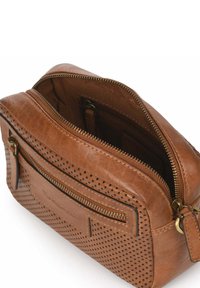 Bruine leren tas met een perforOntwerp, voorzien van gouden hardware, een hoofdvak met rits en een ritsvak aan de voorkant. Het interieur heeft dubbele vakken.