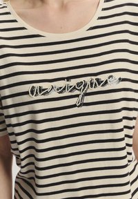 T-shirt w paski w kolorze czarnym i kremowym, z okrągłym dekoltem i krótkimi rękawami, z haftem z koralików i cekinów wyszywającym słowo "unikalny" na klatce piersiowej.