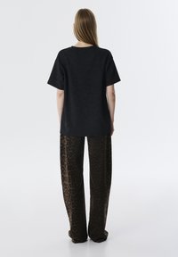 Zwart T-shirt met korte mouwen gecombineerd met een brede bruine broek met luipaardprint, met een ontspannen pasvorm en een gladde stoftextuur.