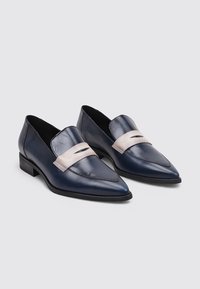 Mocasines de cuero azul marino con punta afilada, que presentan una tira rosa pálido y un detalle recortado en la parte delantera, con un tacón bajo.
