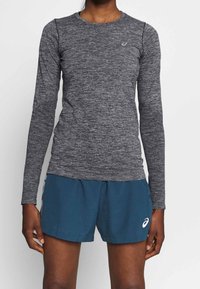 Long-sleeve athletic top in dark gray textured fabric, featuring a round neckline and fitted sleeves. Paired with blue shorts with logo detail.