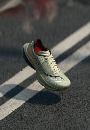Light green running shoe with reflective logo, white laces, and orange interior hovering above a road with white lines.