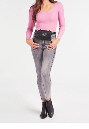 Banane noire zippée portée à la taille ; haut rose à manches longues côtelé ; jean skinny gris délavé ; bottines noires à bouts pointus.