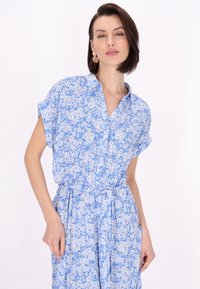 Abito floreale blu, maniche corte, colletto, vita cintrata, tessuto leggero, piccoli fiori bianchi su sfondo blu, include tasche laterali.
