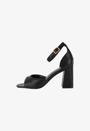 Schwarze, geschlossene Sandale mit Absatz, Knöchelriemen und quadratischen Absatz. Glatte, matte Oberfläche mit einem goldenen Schnallenakzent am Riemen.