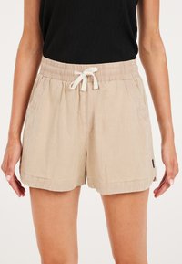 Pantaloni corti intrecciati beige con vita elasticizzata, coulisse, tasche laterali e una vestibilità comoda. Presentano un orlo risvoltato e una leggera texture.