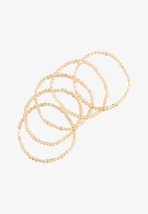 Sechs durchscheinende, beige Perlenelastikarmbänder, überlappend auf weißem Hintergrund angeordnet.