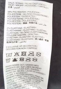Etiqueta de ropa que indica tejido compuesto por 98% poliéster, 2% elastano en varios idiomas, más instrucciones de lavado con los símbolos de cuidado correspondientes.
