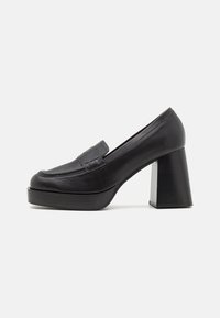 Black leather high-heeled loafer with a rounded toe, decorative strap, and a chunky geometric heel. Smooth texture with minimal stitching details.