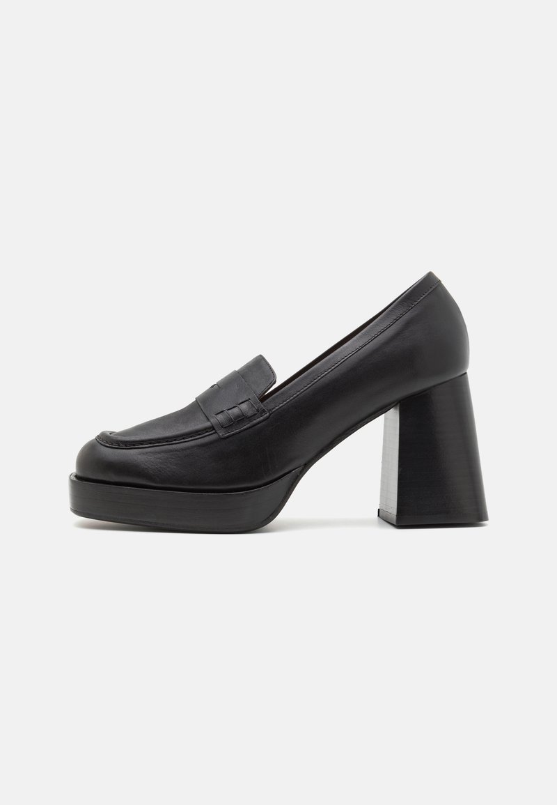Black leather high-heeled loafer with a rounded toe, decorative strap, and a chunky geometric heel. Smooth texture with minimal stitching details.