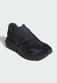 Black athletic shoe with mesh and suede material, purple accents, thick sole, and textured surface; features laces and branding details.