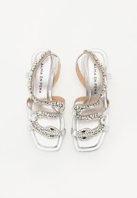 Sølvhelede sandaler med en glatt metallisk finish, korslagte stropper, og dekorert med klare rhinestones og et dekorativt mønster.