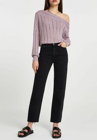 Pull en tricot lavande avec un col asymétrique, associé à un jean noir taille haute à jambes larges. Sandales noires à enfiler avec des accents dorés.