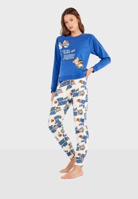 Sweat-shirt bleu avec un motif "Tom et Jerry", associé à un pantalon de pyjama blanc comportant des illustrations répétées des personnages et un texte bleu.