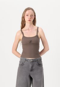 Brun ribbet crop top med tynne stropper og rund hals, med en liten grafisk design i midten. Sammen med grå vide bukser.
