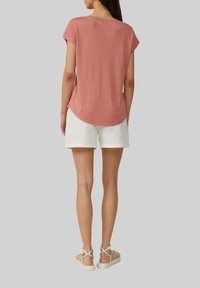 Kokvilnas maisījuma T-krekls putekļu rozā krāsā, īsām piedurknēm, apaļa kakla izgriezums, izliekts apakšmalas dizains. Saskaņots ar baltām lina šortiem un bežām sandālēm ar siksniņām.