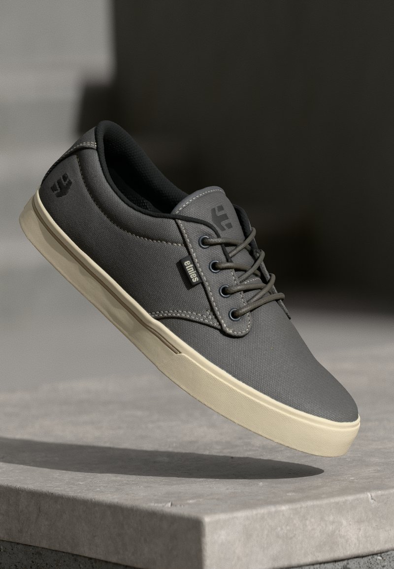 Sneakers in tela grigia con punta arrotondata, design con lacci, superficie texturizzata e suola in gomma color crema, con un logo sulla parte laterale.