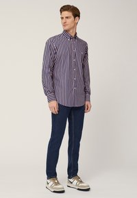 Camicia a righe blu navy e rosa, con maniche lunghe e colletto standard, abbinata a jeans blu scuro e sneaker bicolore.