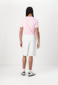 T-shirt rose clair à manches courtes, shorts en jersey gris et baskets grises avec des accents noirs. Design simple, sans motifs ni graphiques visibles.