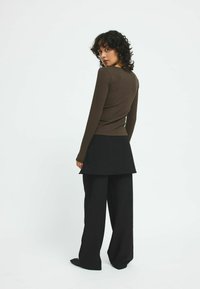 Maglietta marrone a coste con maniche lunghe abbinata a una gonna nera strutturata a strati e pantaloni neri a gamba larga. Design minimalista e colori neutri.
