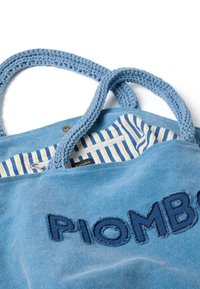 Lichtblauwe tote bag met gevlochten hengsels, met een donkerblauwe geborduurde "PIOMBO" logo. De binnenkant heeft een gele en blauwe gestreepte voering met een ritsvak.