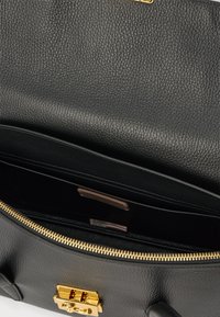 Borsa in pelle nera testurizzata con scomparto aperto, cerniera dorata e chiusura a scatto dorata visibile sulla patta frontale.