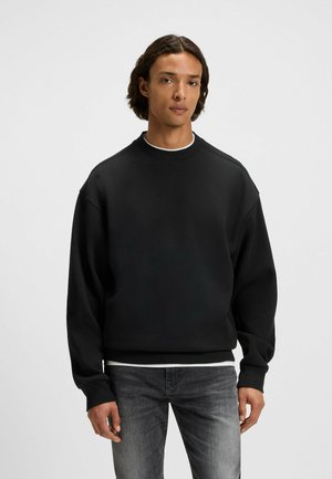 Svart sweatshirt i mjukt material, med rundad halsringning, sänkta axlar och ribbade muddarna. Bärs tillsammans med grå denimjeans.