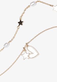 Bracelet en chaîne dorée avec un charme en forme de cœur et d'étoile, agrémenté de perles blanches et d'accents en forme d'étoile entre les maillons de la chaîne.