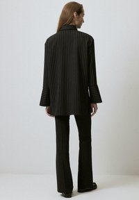 Zwarte pinstripe blazer met een kraag en uitlopende mouwen, gedragen over zwarte uitlopende broeken. Gladde textuur; minimalistisch ontwerp.