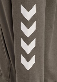 Mörk olivfärgad hoodie med en mjuk textur, med vita chevronmönster tryckta på den högra ärmen.