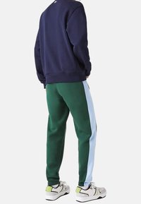 Laivastonsininen collegepaita yhdistetty vaaleansinisellä sivuraitalla varustettuihin vihreisiin collegehousuihin. Asun täydentävät valkoiset ja harmaat lenkkarit, joissa on vihreitä yksityiskohtia.